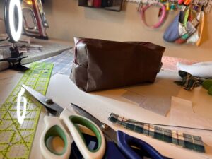 Handmade faux leather toiletry bag with plaid accent and red zipper on messy sewing table