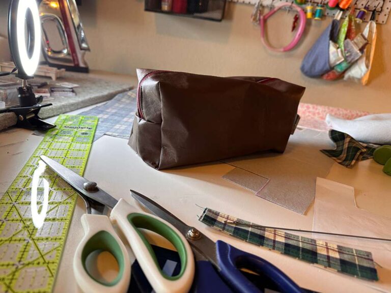 Handmade faux leather toiletry bag with plaid accent and red zipper on messy sewing table