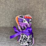 Two packs of handmade makeup remover pads in Disney Villains purple print and Dalmatians print with orange microfiber backing tied with purple ribbon