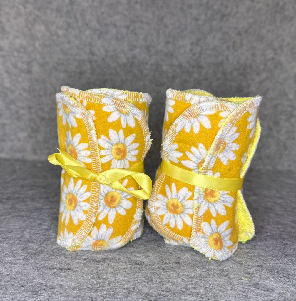Two packs of handmade makeup remover pads in yellow daisy print tied with yellow ribbon showing serged edges and microfiber backing