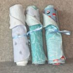 Three Muss Busters Feeling Blue mixed print reusable towel rolls with blue ribbons featuring aquatic, whale, and sushi prints