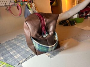 Handmade faux leather toiletry bag with plaid accent and red zipper on messy sewing table